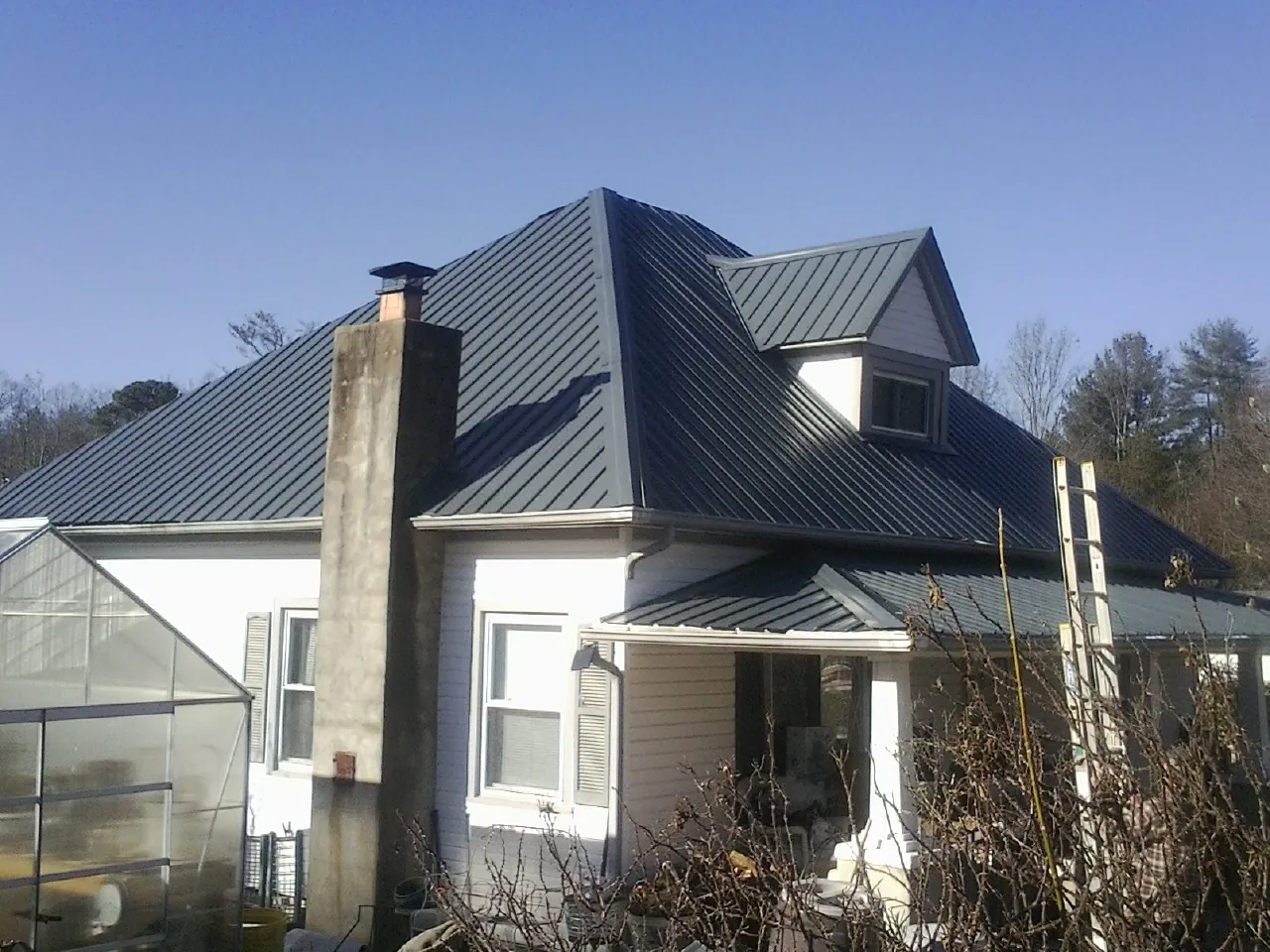 Dark blue standing seam metal roof on a white farmhouse with dormer — Slate & Tile Roof Repair by Roofing Brothers in Camden Wyoming