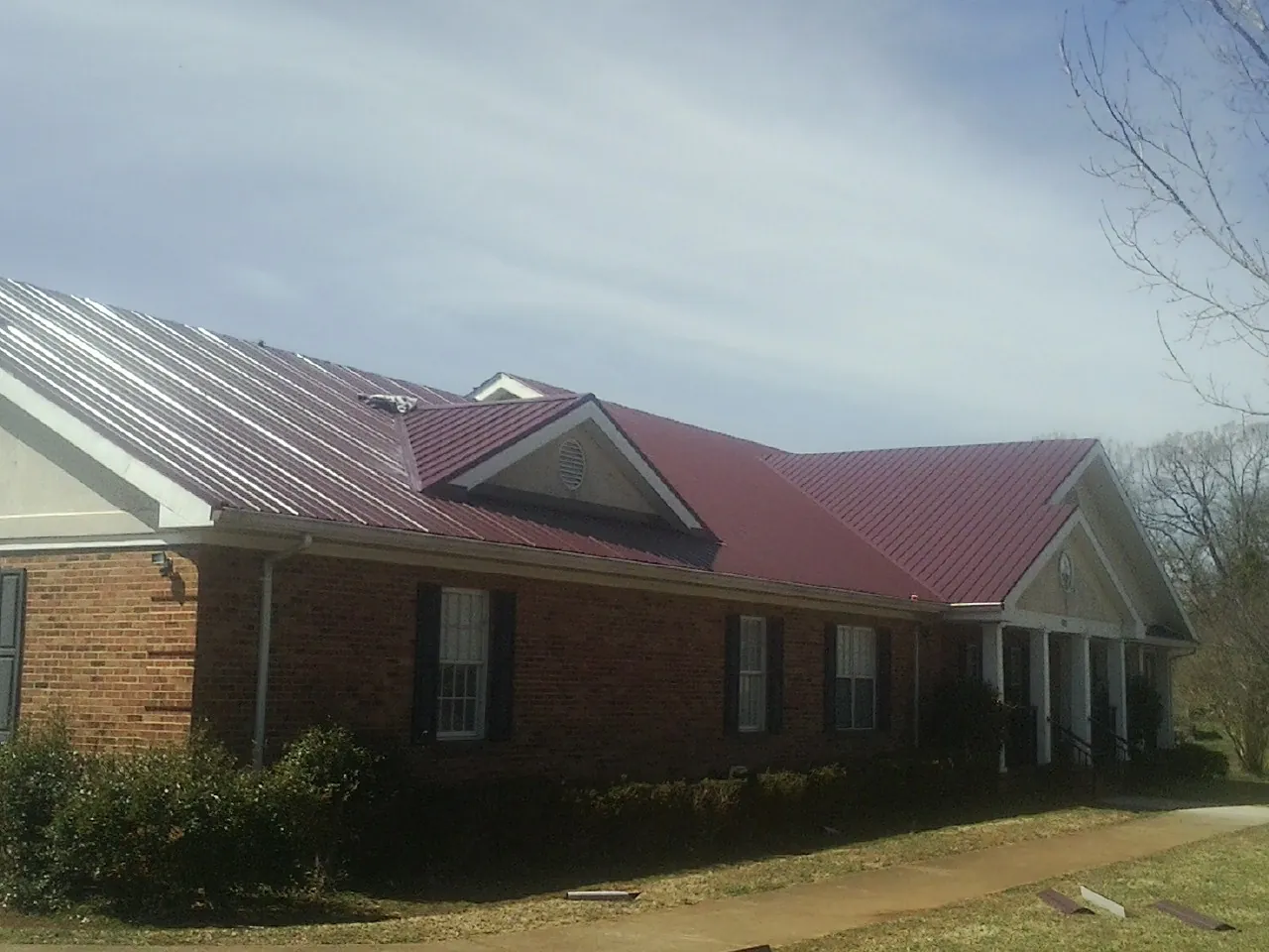 Red metal roof with gabled entries on a long brick building, from a Hail Damage Roof Repair job in Camden Wyoming