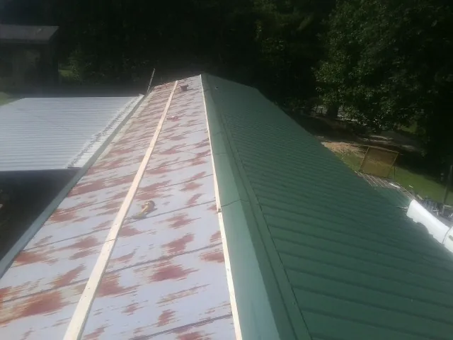 Old rusted panels beside newly installed green metal roofing — Wind Damage Roof Repair by Roofing Brothers in Camden Wyoming