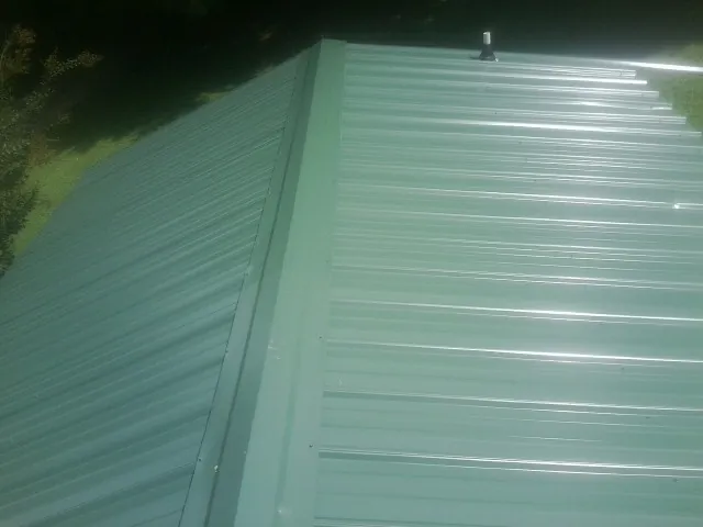 New green metal panels meeting at the ridge of a roof — Flat Roof Repair work by our crew in Camden Wyoming