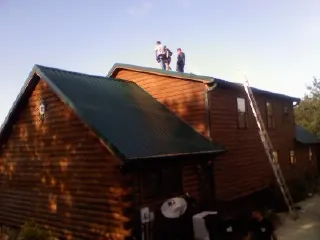 Crew on the ridge of a green metal roof on a two story log home in Camden Wyoming
