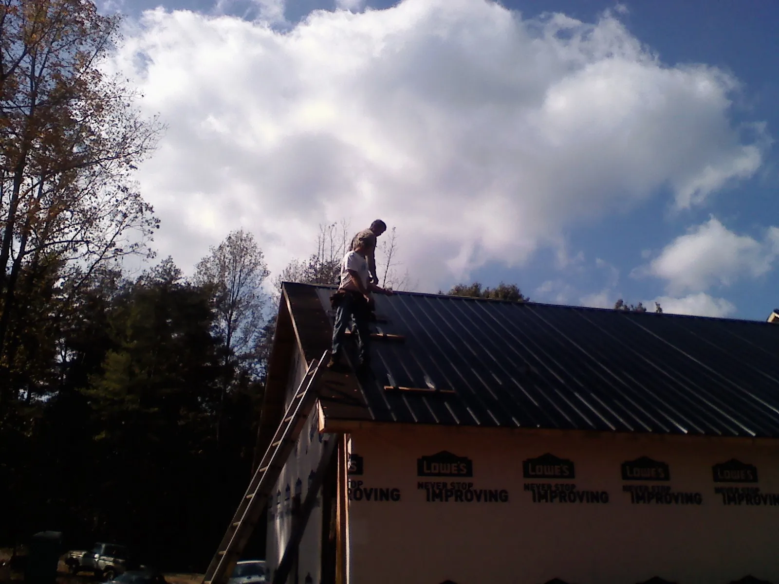 Roofer fastening dark metal panels high against a cloudy sky, from a Roof Inspection job in Camden Wyoming