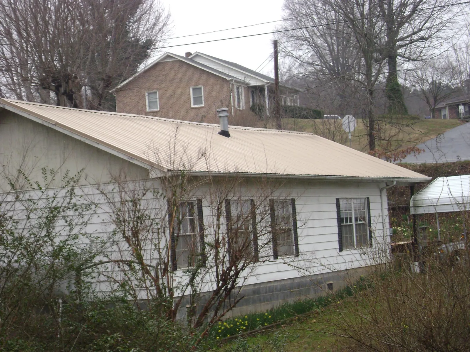 Tan metal roof on a white sided house set into a hillside — Commercial Roofing by Roofing Brothers in Camden Wyoming