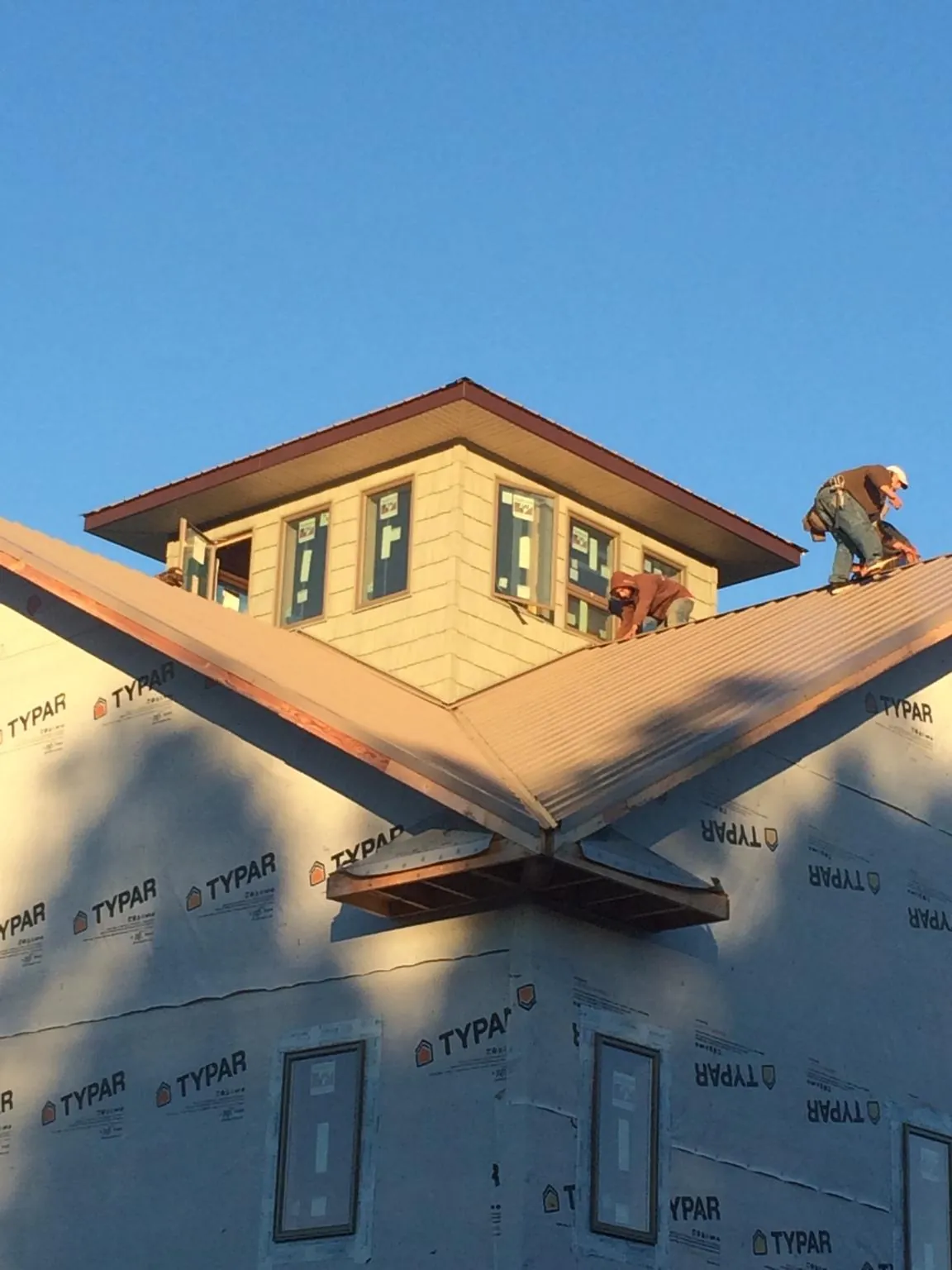 Roofers working around a rooftop cupola on a new metal roof at sunset — Roof Waterproofing in Camden Wyoming by Roofing Brothers